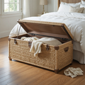 Woven storage chest in a bedroom with white bedding and a lamp.